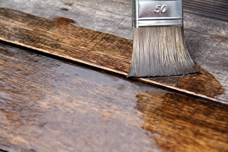Pinceau appliquant un produit de traitement sur planches de bois vieillies en extérieur