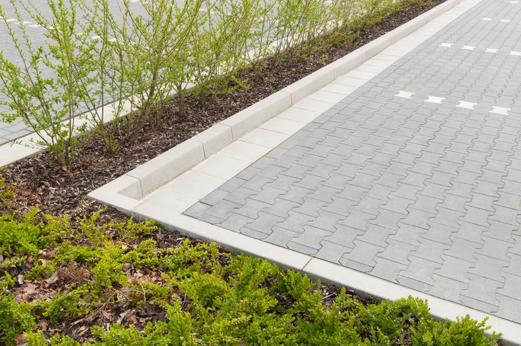 Aménagement paysager extérieur avec allée pavée en béton délimitée par bordures blanches préfabriquées
