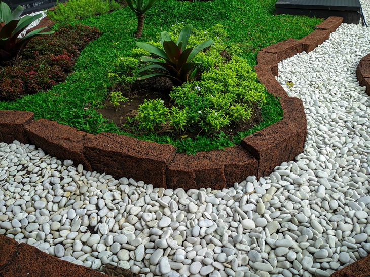 Jardin extérieur avec massif fleuri surélevé délimité par muret en pierre reconstituée beige
