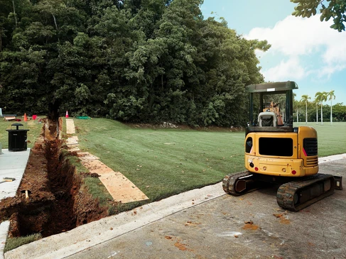 Chantier ext&eacute;rieur d'am&eacute;nagement paysager avec excavatrice compacte jaune positionn&eacute;e sur dalle b&eacute;ton