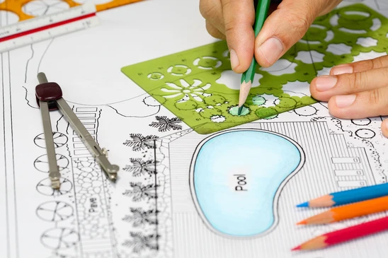 Une personne dessine sur un plan d'am&eacute;nagement paysager avec un crayon vert, coloriant une zone v&eacute;g&eacute;talis&eacute;e