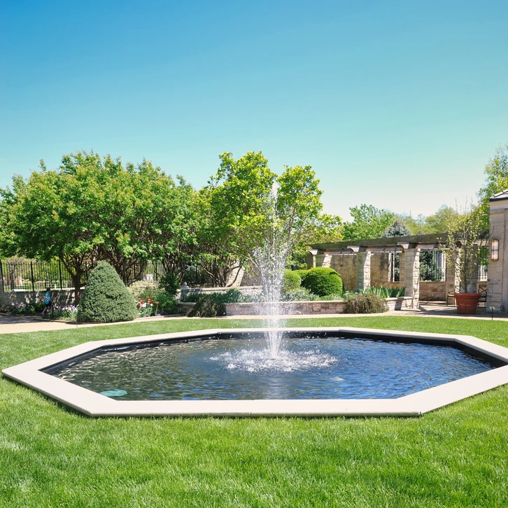 Jardin paysager avec bassin d'ornement circulaire et jet d'eau central sur pelouse entretenue