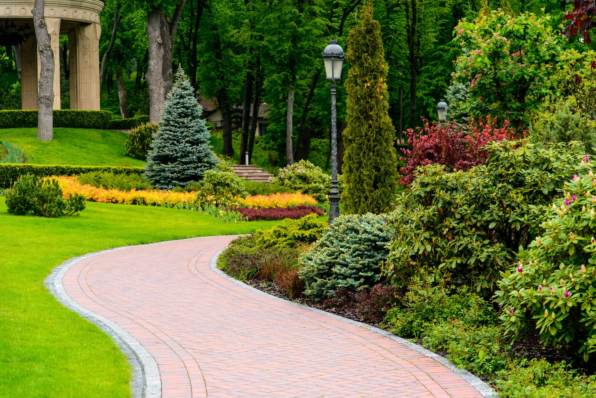 Jardin paysager en terrasses avec parterres de fleurs colorées disposés en motifs géométriques, allées courbes pavées, pelouses entretenues et arbustes taillés